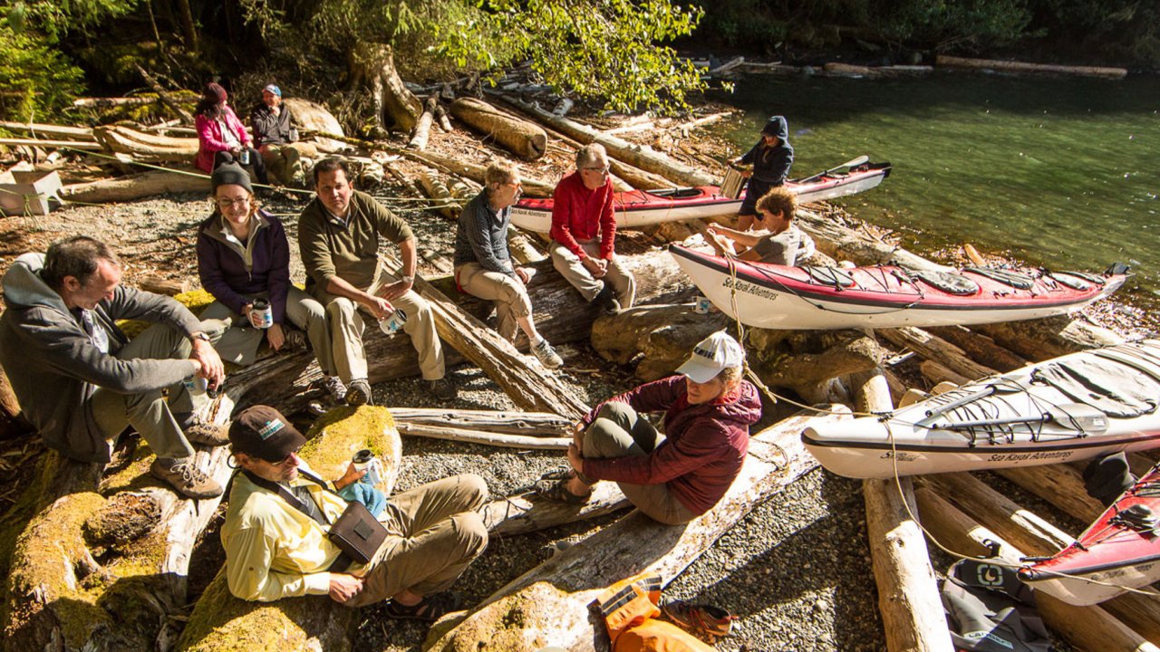 people and sea kayaks resting on log pile