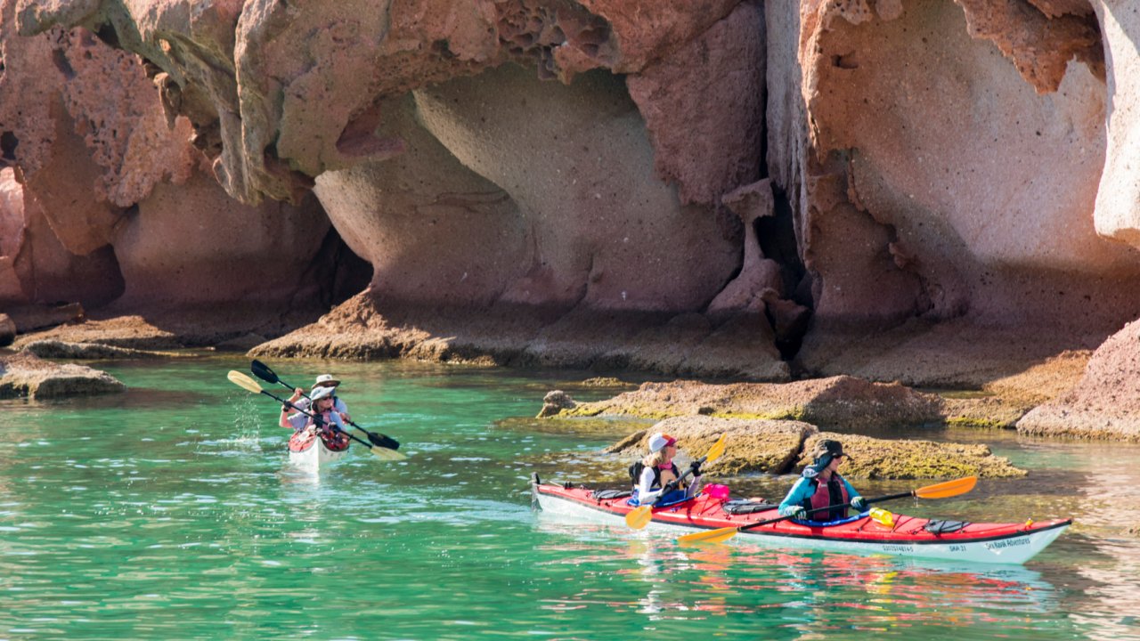 sea kayaks in blue water with rock formations behind