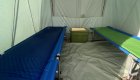Inside of a canvas style tent with two cots and two sleeping pads set up on either side of the tent.