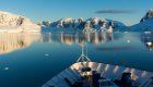 The bow of a small cruise ship headed towards glaciers and ice bergs on a sunny day in Antarctica