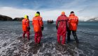 4 people in protective suites walking through the water to get back to their raft in Antarctica