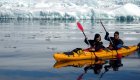 Two people in a yellow tandem sea kayak paddling through icebergs