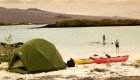 A green tent on a beach with two kayaks and two people standing in the water in the Galapagos Islands