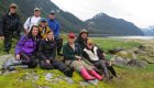 A group of hikers sitting and standing on a rock in a green grass field on a misty day in Alaska