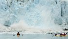 Two yellow sea kayakers paddling towards massive icebergs and glaciers in Alaska