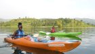 Two travelers kayaking on calm water at Lake Kivu with rolling green hills behind them.