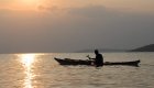 Kayaker paddling across calm water at sunset on Lake Kivu with distant hills on the horizon.