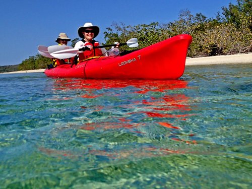A red tandem sea kayak with people paddling and smiling off the shores of Cuba