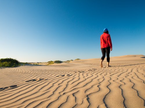 Traveler walking barefoot across rippled desert sand dunes under a bright blue Baja Mexico sky, capturing the stillness and beauty of Mexico’s wilderness.