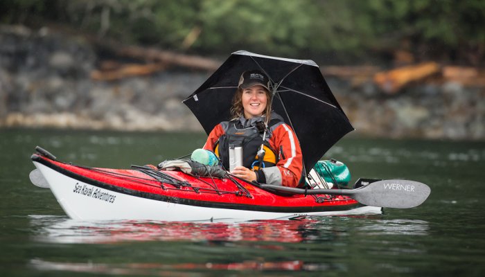 A girl in a red sea kayak holding a coffee cup and an umbrella 