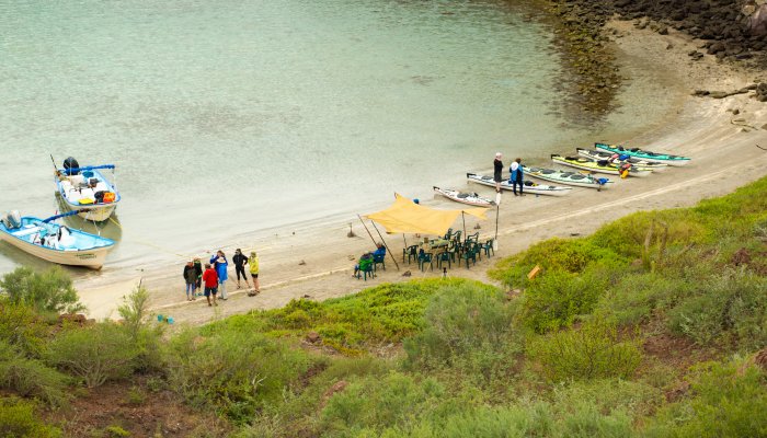 Two small panga boats anchored to a beach in Loreto Bay National Park with sea kayaks on shore and peoples walking around